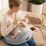 New mom smiling while breastfeeding baby on gray Momcozy Original nursing pillow in sunny living room
