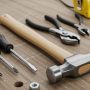 A neatly organized set of essential hand tools including a hammer, screwdrivers, pliers, and tape measure laid out on a wooden workbench