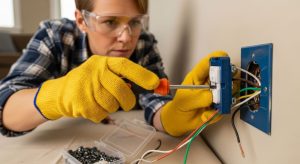 A DIY homeowner wearing safety gear electrical gloves and glasses while using insulated tools to replace a wall outlet