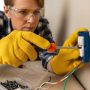 A DIY homeowner wearing safety gear electrical gloves and glasses while using insulated tools to replace a wall outlet