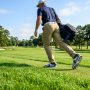 Golfer walking on green grass fairway wearing supportive white golf shoes.
