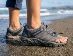 : Close-up of feet wearing flexible mesh swim shoes on sandy beach.