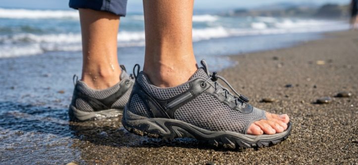 : Close-up of feet wearing flexible mesh swim shoes on sandy beach.