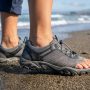 : Close-up of feet wearing flexible mesh swim shoes on sandy beach.