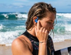 Surfer adjusting secure silicone surf ear plug before heading into ocean waves.