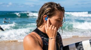 Surfer adjusting secure silicone surf ear plug before heading into ocean waves.