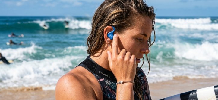 Surfer adjusting secure silicone surf ear plug before heading into ocean waves.