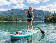 Person standing and paddling on an inflatable paddle board on a calm lake.